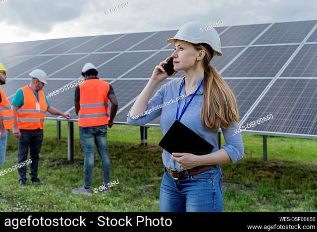 Woman talking on mobile phone with coworkers in background at solar station