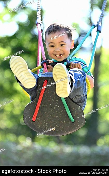 toddler, 2 years, multiethnic, eurasian, laughs, swings on a children's swing, blaubeuren, baden-württemberg, germany