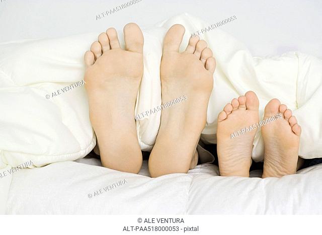 Parent and child's bare feet sticking out from under comforter, close-up