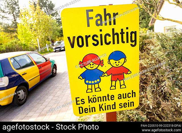10 May 2022, Mecklenburg-Western Pomerania, Born: A sign with the lettering "" Drive carefully - It could also be your child"" stands in sunny weather as a car...