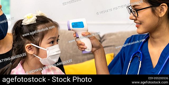 Panoramic Asian female doctor use infrared thermometer to take temperature to little girl child in living room while doctor visit at home