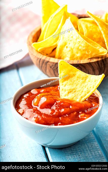 Corn nacho chips and tomato dip. Yellow tortilla chips and salsa on old blue table