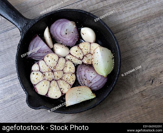 Slices of garlic, red and yellow onion in a frying pan with spices, on wooden background. Top view