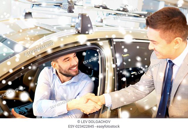 auto business, car sale, consumerism, gesture and people concept - happy man with car dealer making deal and shaking hands in auto show or salon over snow...