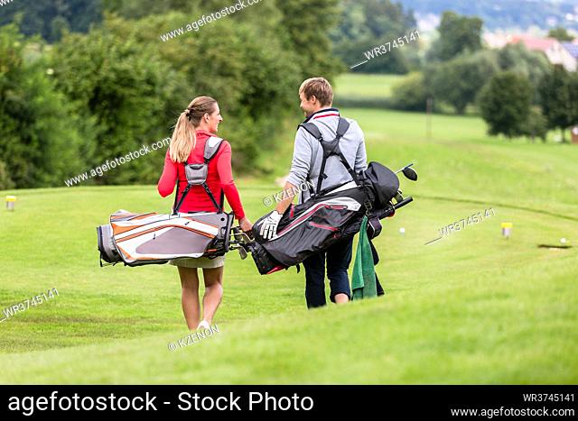 Rear view of golfing couple carrying their bag walking and chatting on golf course