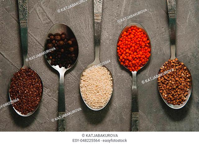 Spoons with different superfoods - flax seeds, sesame, pepper, red lentils, buckwheat on a gray background
