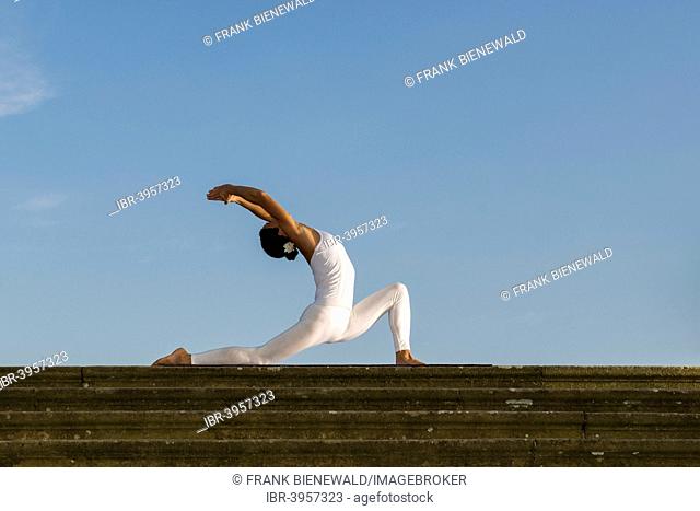 Young woman practising Hatha yoga, outdoors, showing the pose Anjaneyasana, Chandrasana, Half moon pose