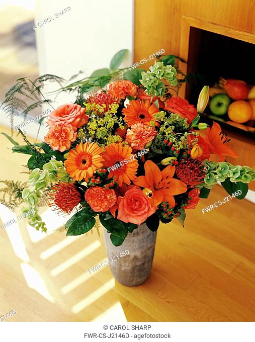 Carnation, Dianthus, Floral arrangment with Gerberas, Oriental Lilies and Bells of Ireland in a vase on a wooden floor
