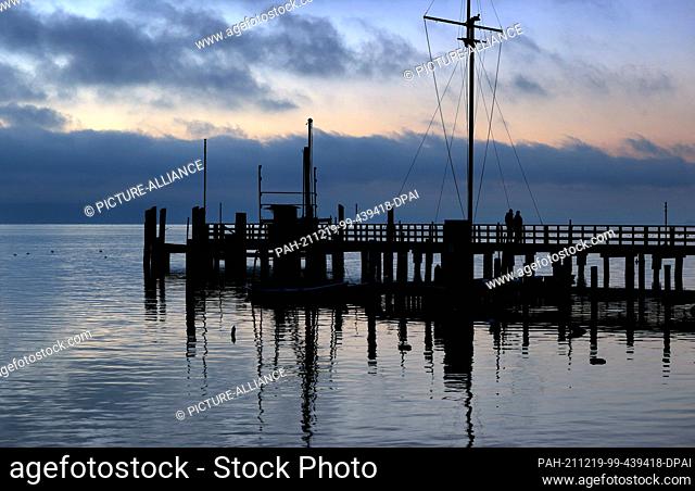 19 December 2021, Bavaria, Utting: Two women are walking on a jetty at the Ammersee shortly before sunrise. Photo: Karl-Josef Hildenbrand/dpa