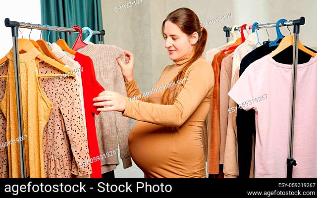 Beautiful pregnant woman choosing what to wear today. Yougn woman expecting baby looking on dress hanging on clothes rack