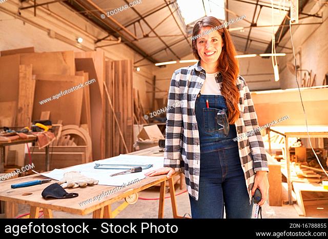 Zufriedene junge Frau als Schreiner Lehrling in der Werkstatt der Tischlerei