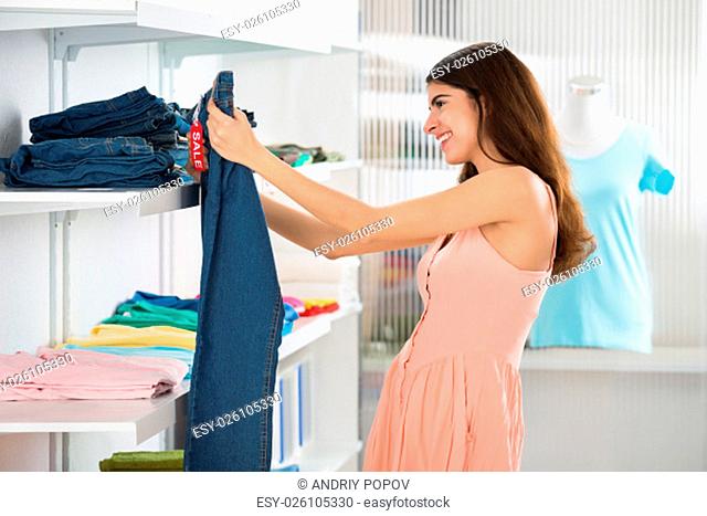Beautiful young woman choosing jeans in store