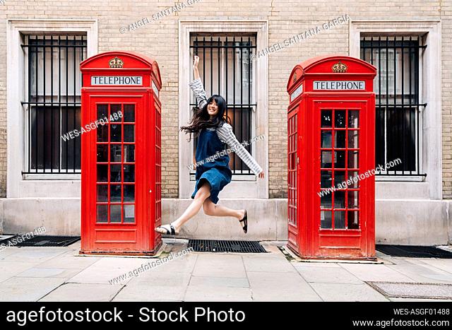 Carefree woman jumping in front of telephone booth