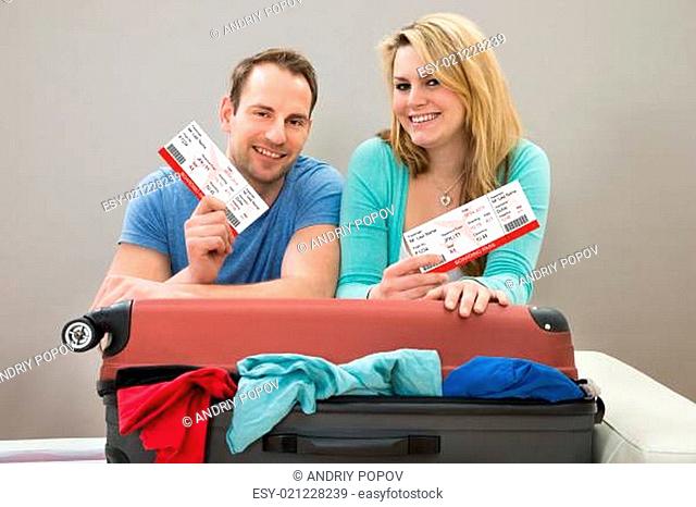 Portrait Of Happy Couple With Boardingpass Leaning On Suitcase