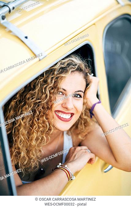 Portrait of happy blond woman looking out of window of classic car