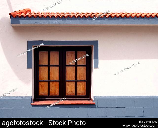 traditional old wooden window with glass panes closed internal shutters on a clean white house wall with gray painted surround and lower area with clay tiled...