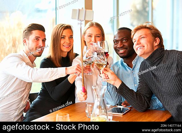 Junge Leute im Restaurant stoßen an mit Wein und machen davon ein Selfie