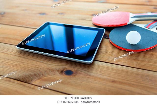 sport, technology, game and objects concept - close up of ping-pong or table tennis rackets with ball and tablet pc computer on wooden floor