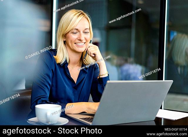 Smiling freelancer using laptop sitting in coffee shop