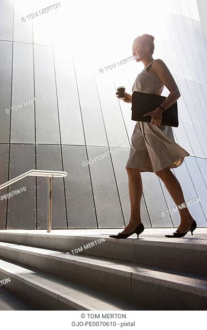 Businesswoman with coffee walking down steps outdoors
