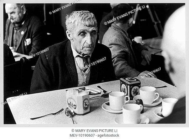 An old man, careworn and tired sits at the tea table in an Old People's Home in Daventry