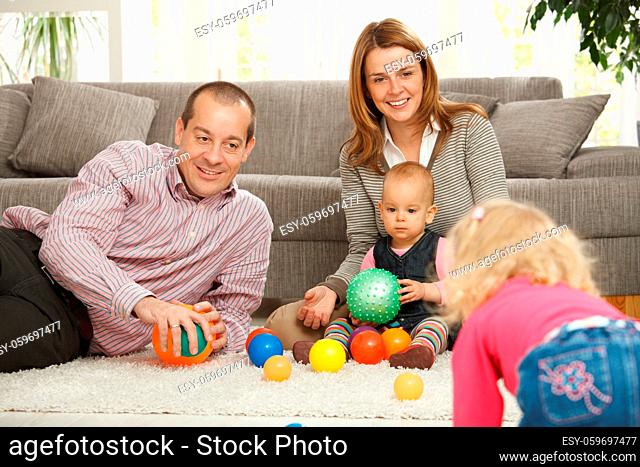 Smiling family of four playing with balls on living room floor