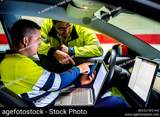Male technician discussing over mobile phone while programming in electric car