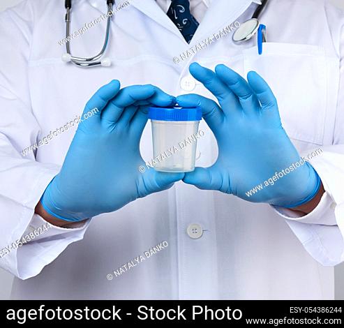 male doctor in a white coat and tie stands and holds a plastic container for urine specimen, wearing blue sterile medical gloves
