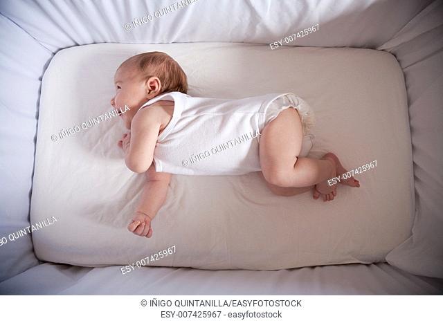 one month age newborn baby laughing lying in white cradle sheet