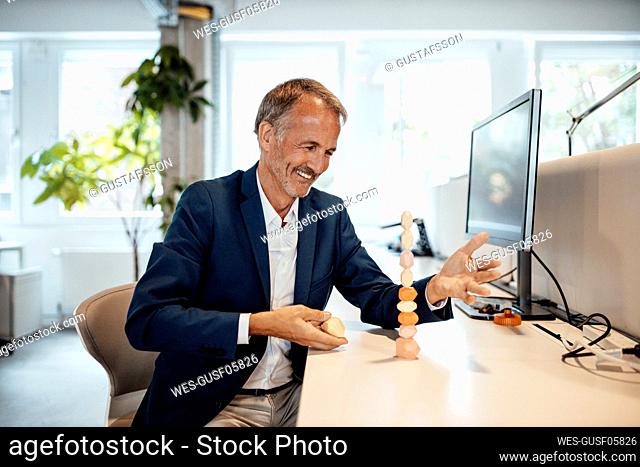 Smiling businessman looking at stack of wooden rock at office