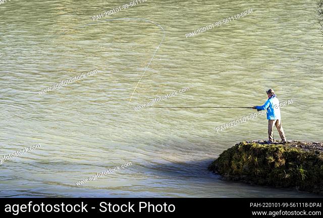 01 January 2022, Bavaria, Munich: A man with stands in spring temperatures on a ledge at the Isar and fishes. Photo: Peter Kneffel/dpa