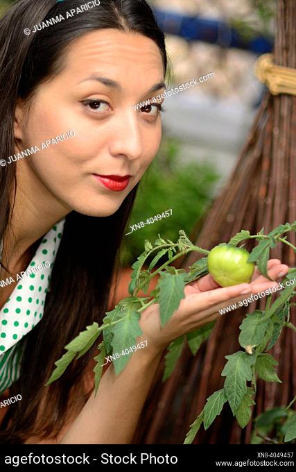 Portrait of young woman looking at camera and green tomato on her hand
