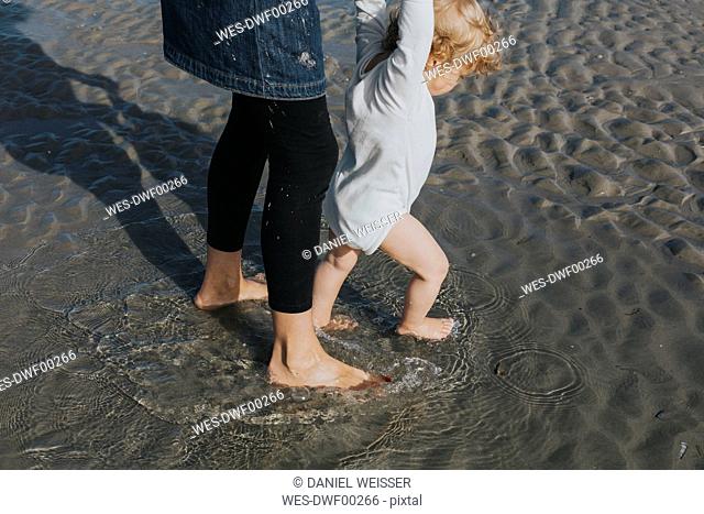 Mother with little daughter wading in water on the beach