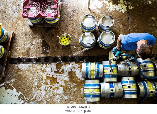 Directly above view of a man working in a brewery, metal beer kegs standing on the floor