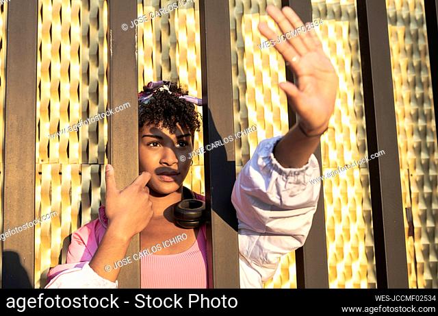 Woman shielding eyes while holding metal structure during sunny day
