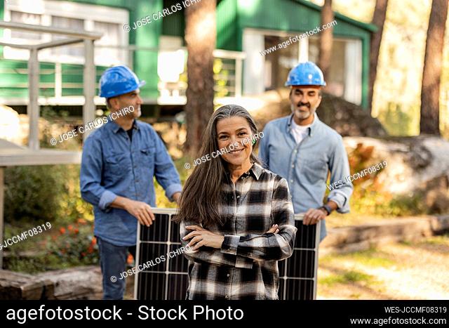 Home owner standing in front of photovoltaic technicians with arms crossed