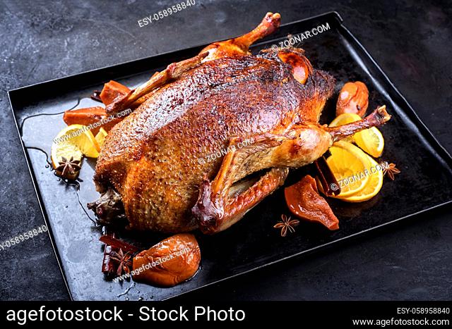 Traditional roasted stuffed Christmas duck with quinces and orange slices served as close-up on a rustic metal tray on a black board