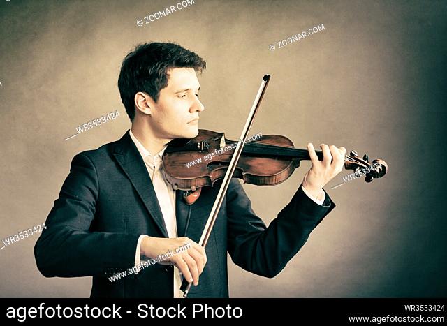Art and artist. Young elegant man violinist fiddler playing violin on brown. Classical music