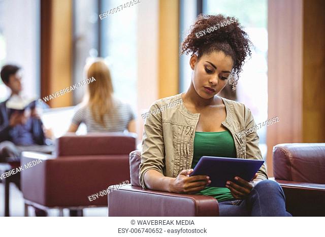 Focused student sitting on sofa using her tablet pc