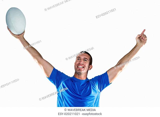 Happy rugby player in blue jersey holding ball with arms raised