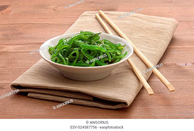 White bowl with chuka seaweed on the napkin with wooden chopsticks