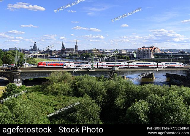 13 July 2020, Saxony, Dresden: An S-Bahn and an IC run in front of the historical old town scenery with the Frauenkirche (l-r), the Ständehaus, the Hofkirche