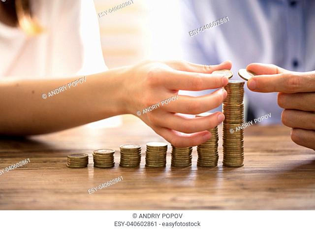 Couple Stacking Golden Coins Over Wooden Desk