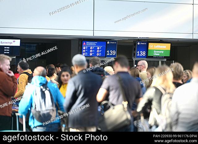 30 September 2022, North Rhine-Westphalia, Duesseldorf: Travelers at Düsseldorf Airport stand in lines at the counters in the departure hall