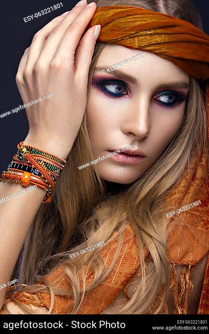 Beautiful fashion girl in a scarf and bracelets boho style. Beauty face, bright trendy makeup. Picture taken in the studio