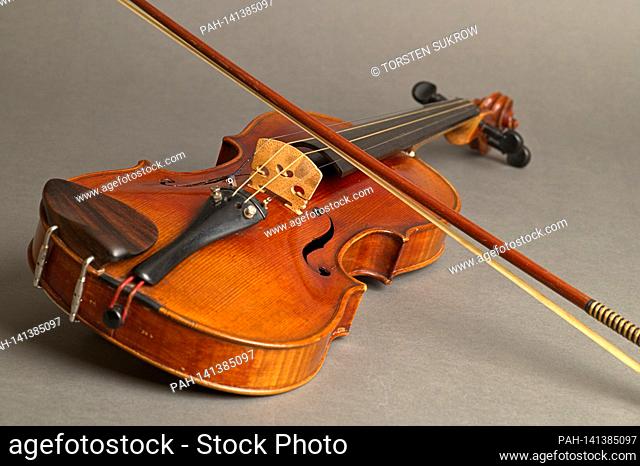An old violin with slight scratches and damage with bow lying on a neutral gray background. | usage worldwide. - /Deutschland
