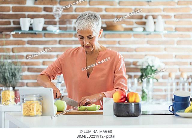 Older Caucasian woman cutting apples in kitchen