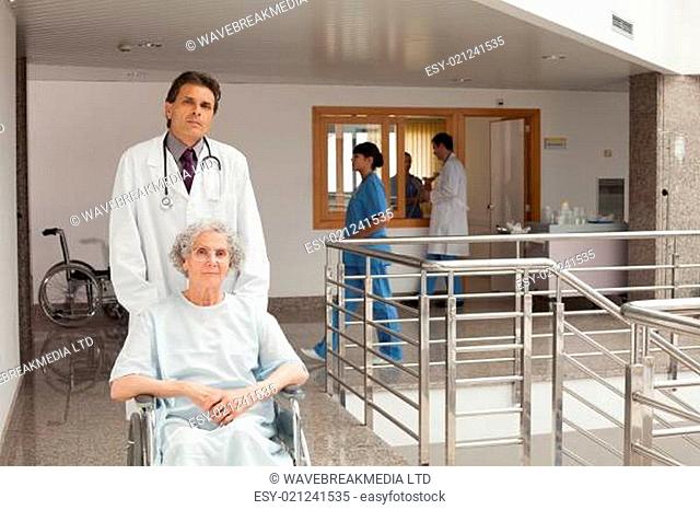 Old woman sitting in a wheelchair while the doctor is pushing in hospital corrid