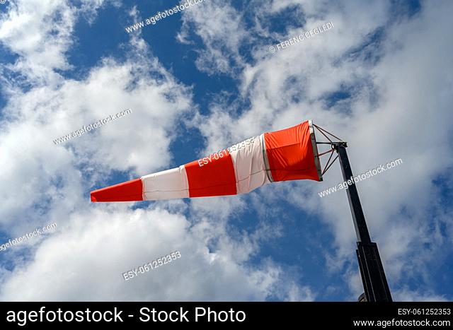 Red and white striped windsock waving in the wind over blue and cloudy sky