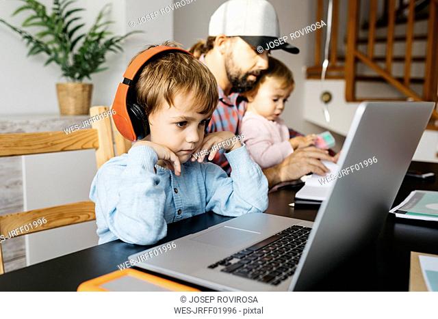 Father working at home, using laptop with his children on his lap